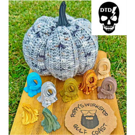 Knitted pumpkin on a wooden board with colorful yarn balls and a brand logo in the corner.