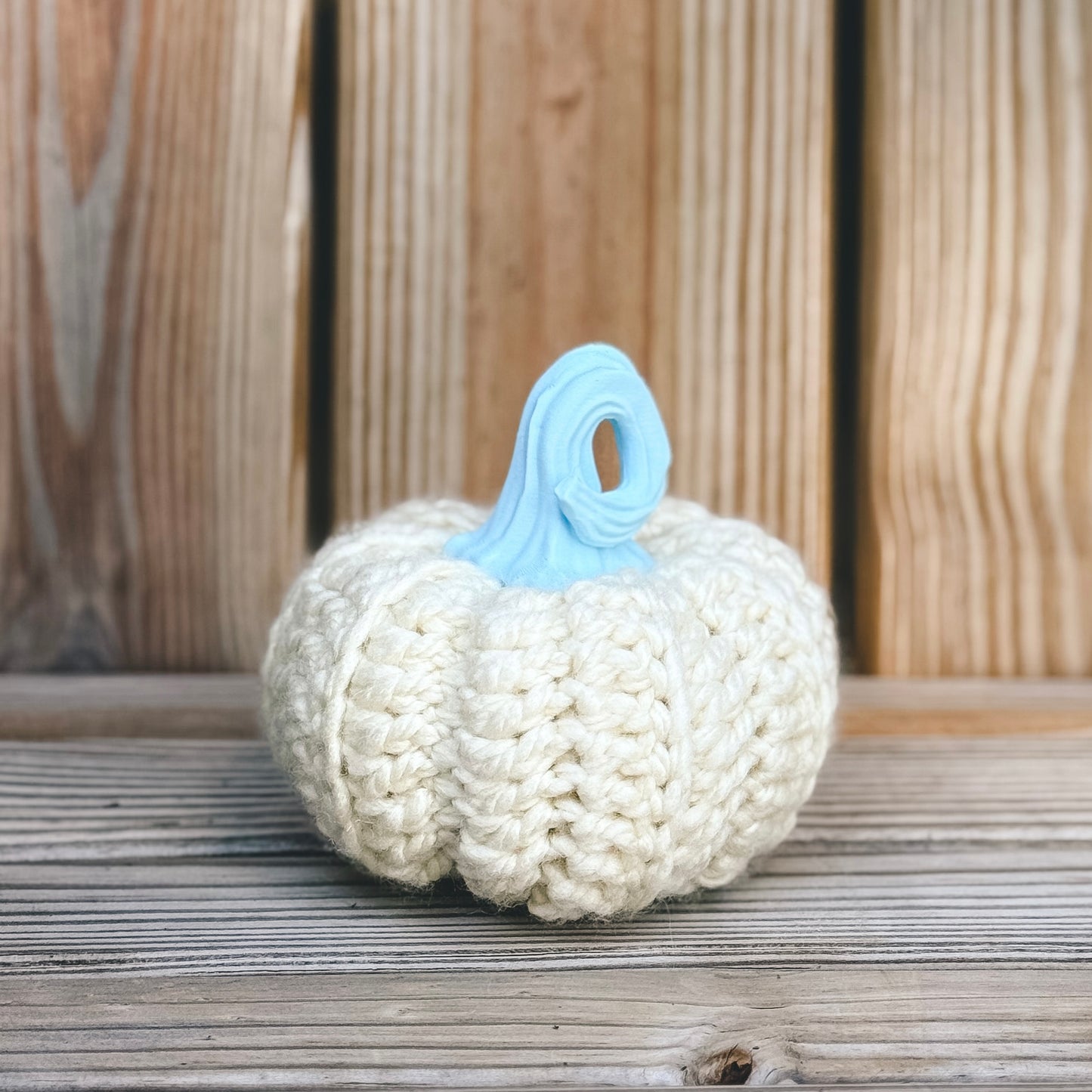 Knitted pumpkin with a blue stem on a wooden surface