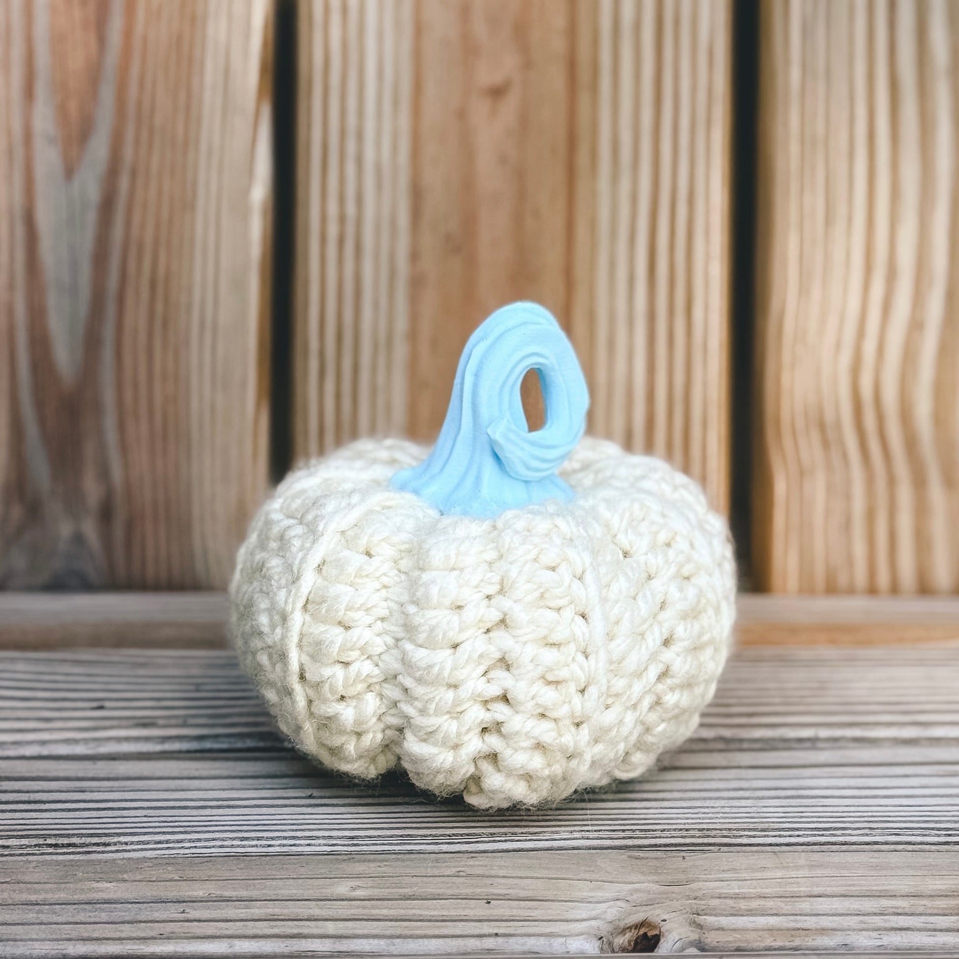 Knitted pumpkin with a blue stem on a wooden surface