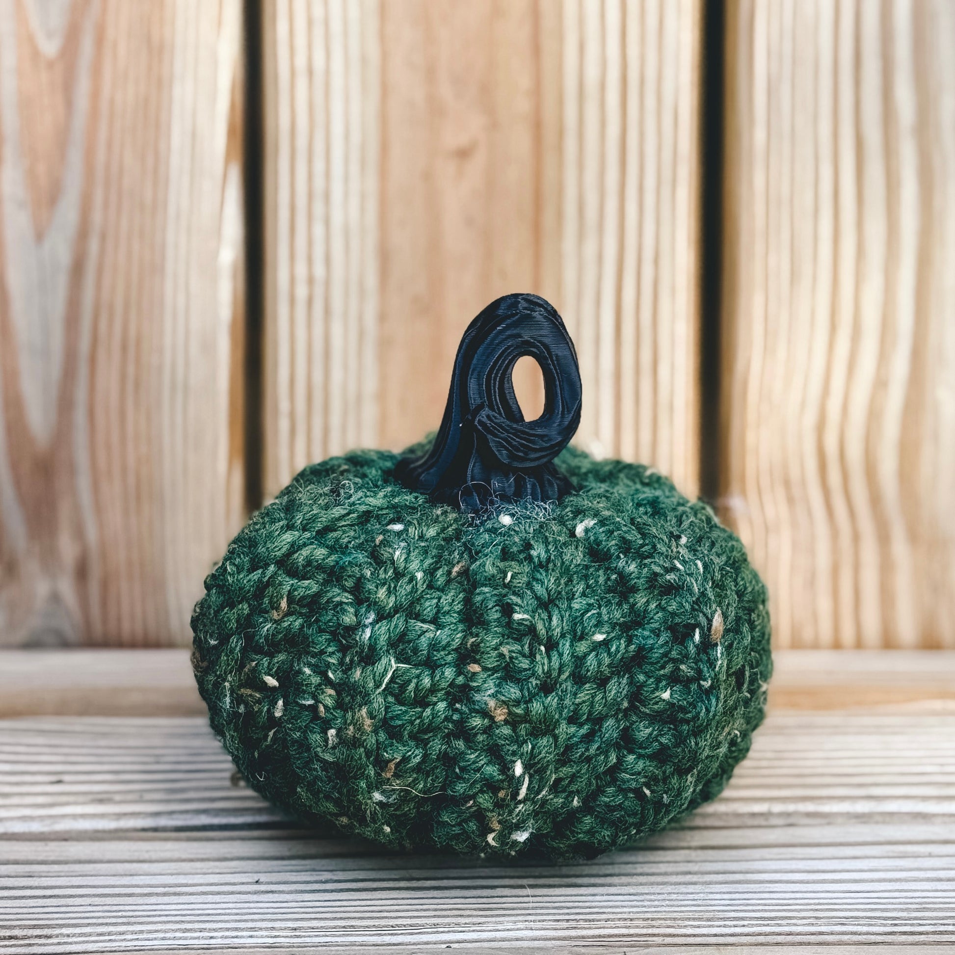 Green crocheted pumpkin with a black stem on a wooden surface