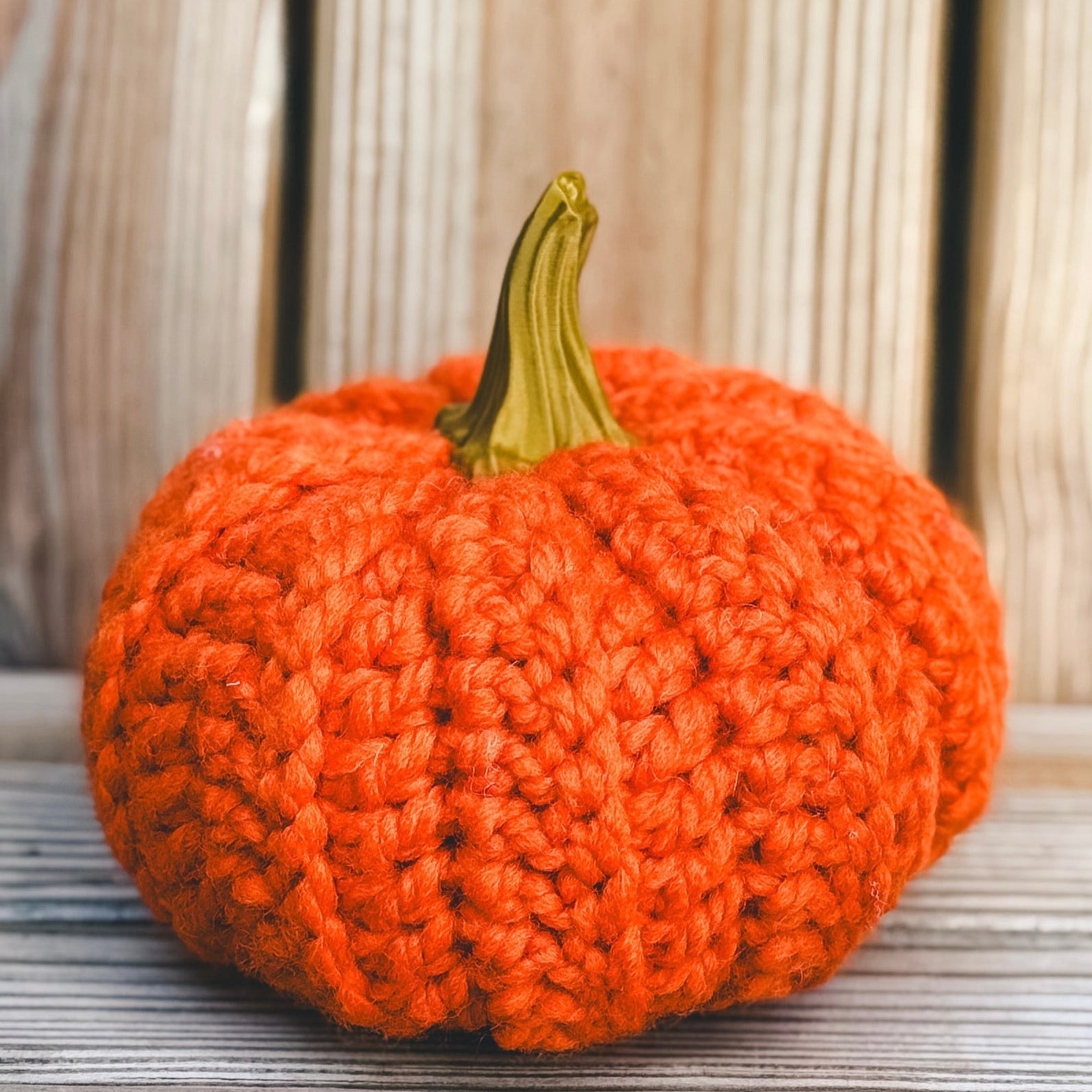 Knitted pumpkin on a wooden surface with a wooden background