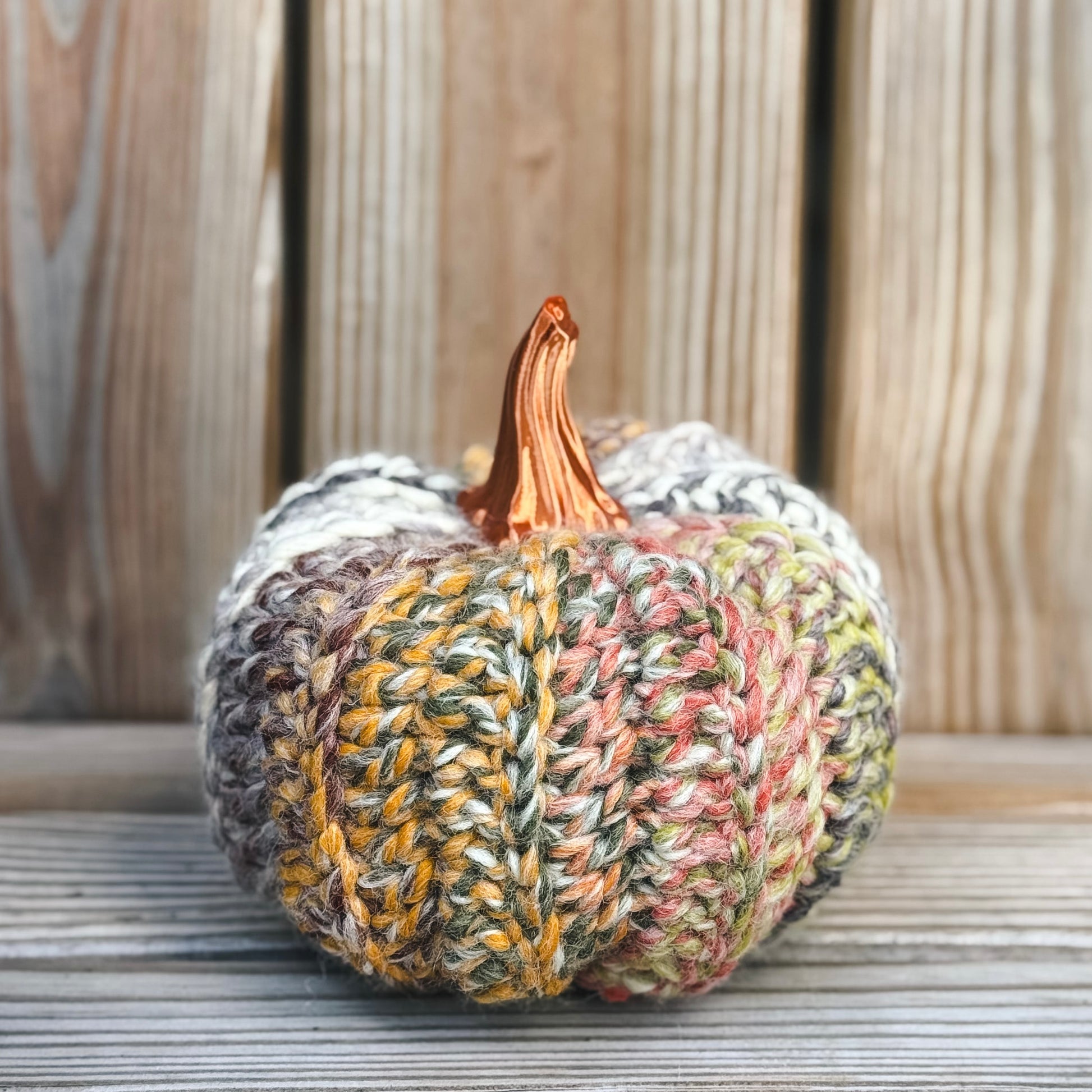 Knitted pumpkin with a wooden stem on a wooden surface