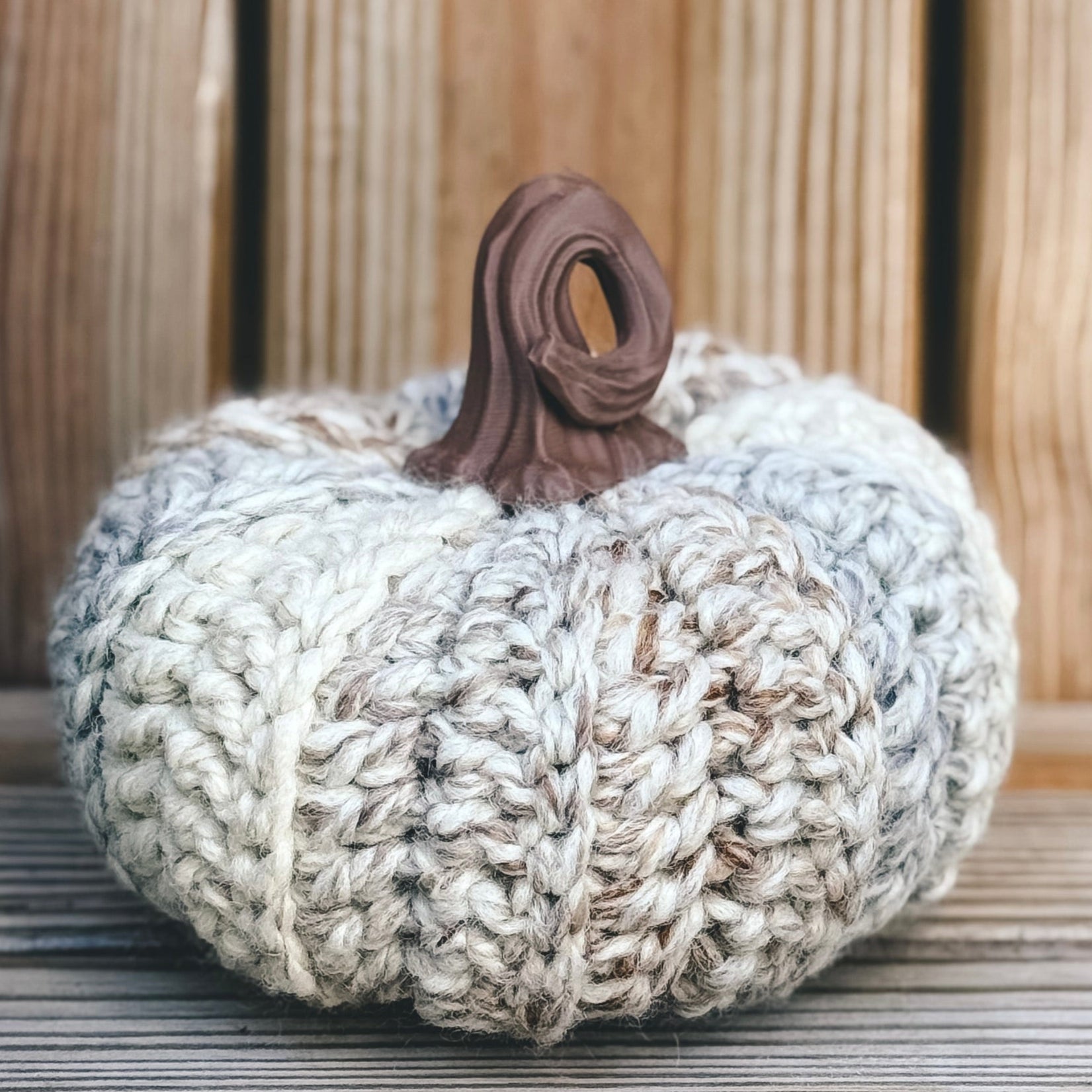 Knitted pumpkin decoration on a wooden surface with a wooden background