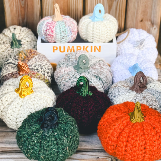 Collection of crocheted pumpkins in various colors on a wooden surface.