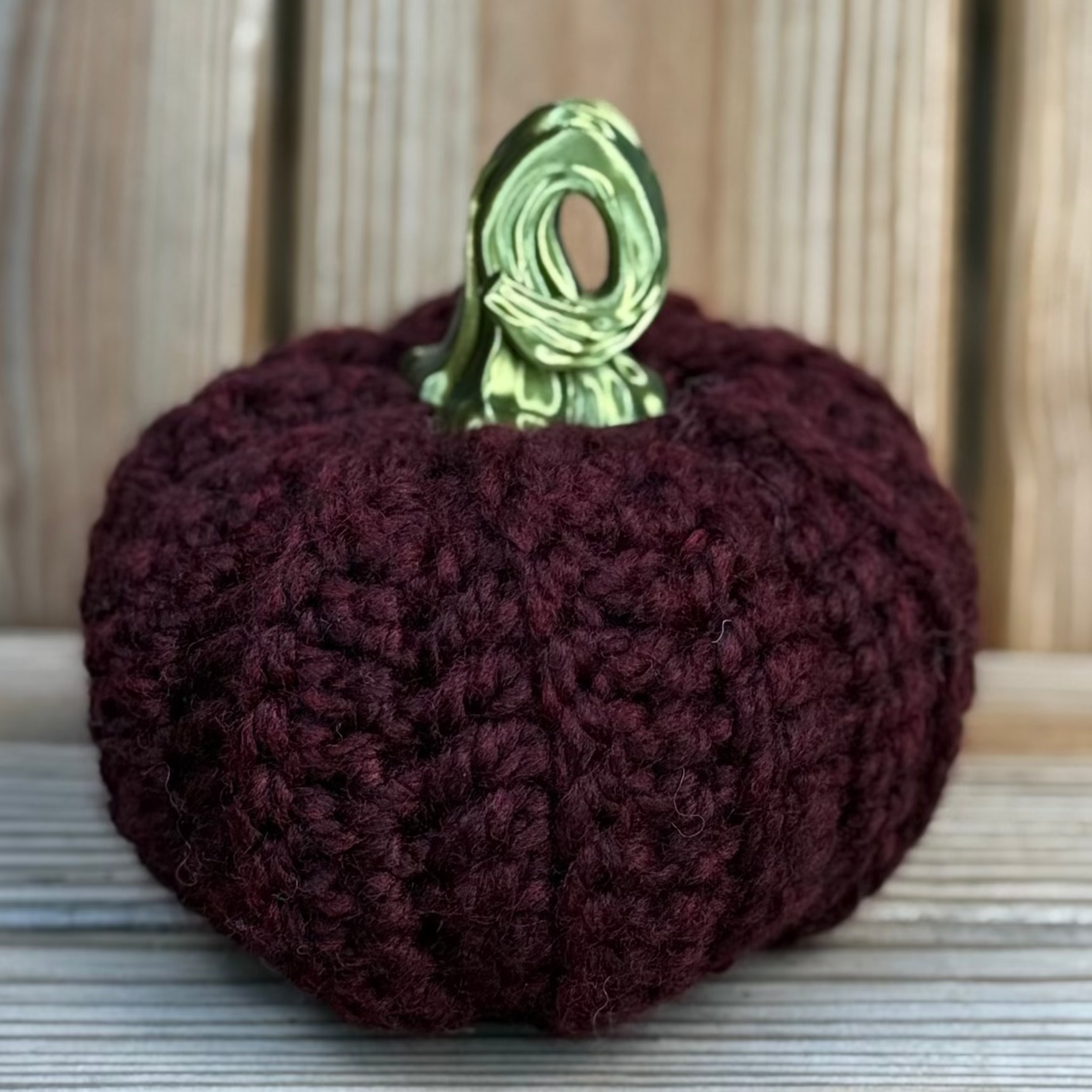 Crocheted purple pumpkin with a green stem on a wooden surface