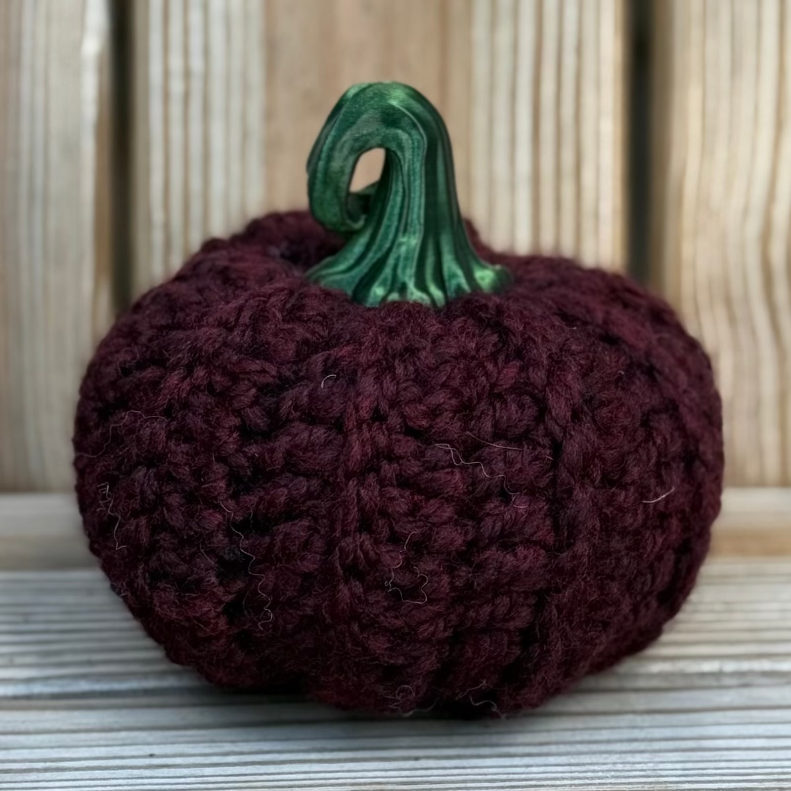 Knitted pumpkin with a green stem on a wooden surface