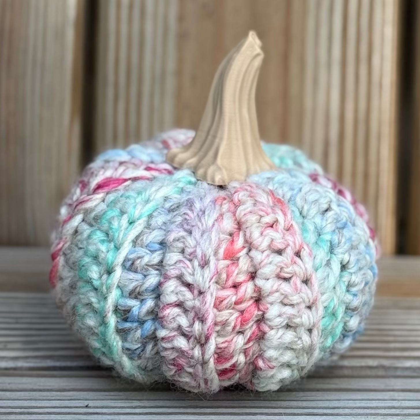 Knitted pumpkin with pastel colors on a wooden surface