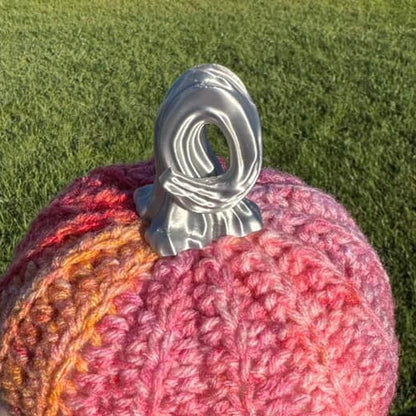 Crocheted pink and orange yarn ball with a silver stem on grass